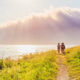 a picture of 2 pilgrims walking along the sea on a path